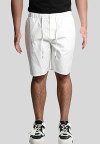 Shorts bianchi in cotone con vita elasticizzata e cordoncino. Design a gamba dritta con una superficie liscia. Indossati con sneakers in bianco e nero.