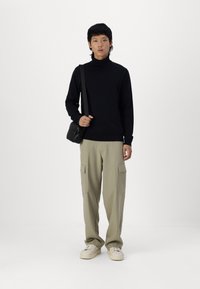 Suéter negro de cuello alto, pantalones cargo beige con bolsillos laterales, zapatillas blancas y un pequeño bolso negro crossbody. Diseño simple y moderno.