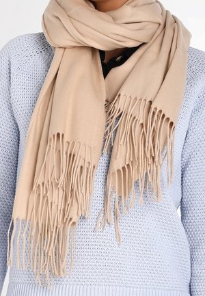 Écharpe beige à franges enroulée autour du cou sur un pull en tricot bleu clair, avec un aperçu d'une chemise noire en dessous.