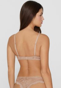 Beha met veterachterkant in naaktkleur met verstelbare bandjes, voorzien van delicate bloemenpatronen en een haak-en-oogsluiting voor een veilige pasvorm.