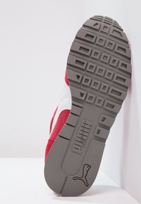 Semelle de sneaker rouge et blanche, avec une texture en caoutchouc et une prise à motif. Détails de la marque et quincaillerie visibles près de la zone du talon.