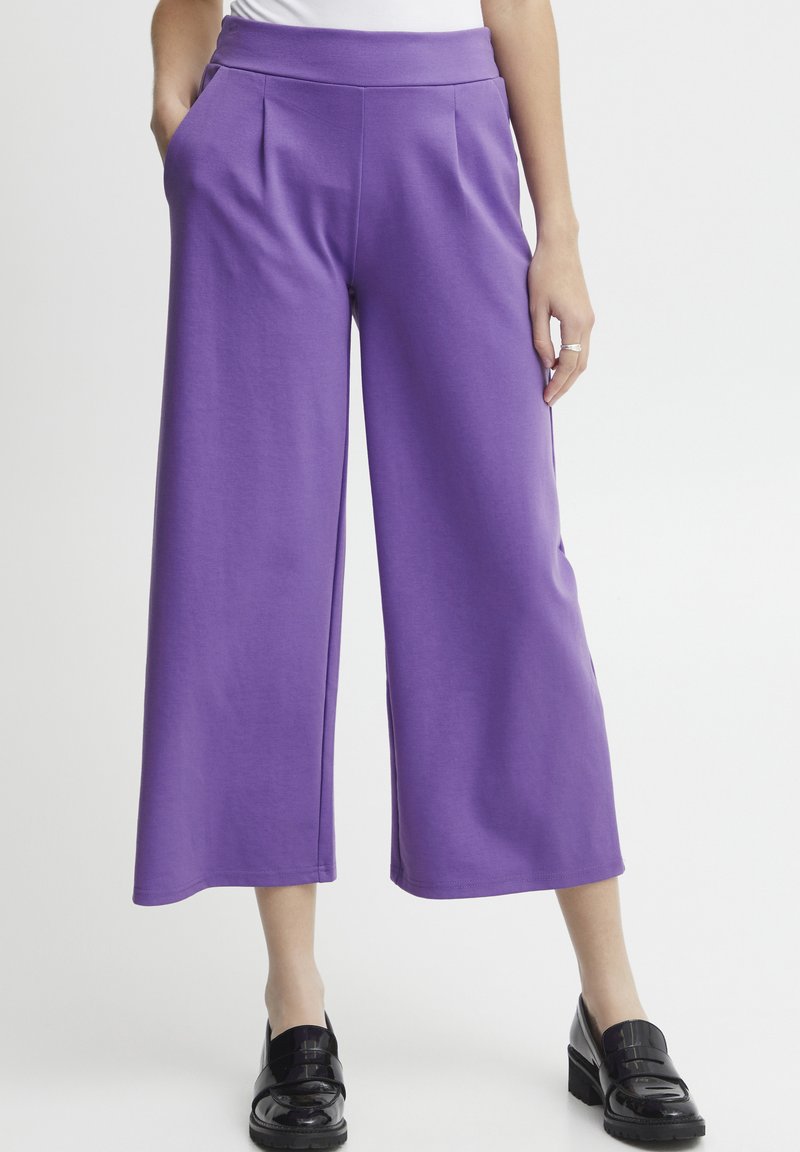 Pantaloni larghi viola realizzati in un tessuto liscio. Presentano una vita alta, tasche laterali e una silhouette rilassata. Abbinati a scarpe nere.
