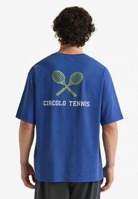T-shirt in cotone blu con un grafiche di racchette da tennis incrociate in verde e il testo "CIRCOLO TENNIS" sottostante.