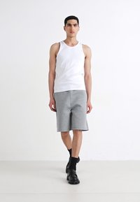 Bílý bezrukávový top kombinovaný se šedými šortkami po kolena, nošený s černými ponožkami a masivními černými botami. Jednoduchý, sportovní design.