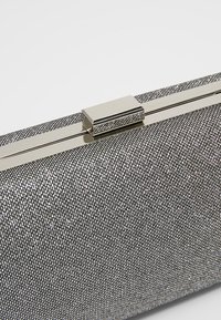 Pochette avec une surface texturée métallique argentée, ornée de petits détails réfléchissants, et une fermeture à boucle argentée élégante.