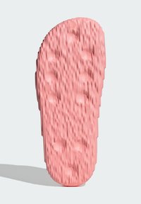 Sohle einer pinkfarbenen Gummisandale mit strukturierten Rippen und gemusterten Punkten für besseren Halt. Abgerundete Form mit glatter Oberfläche.