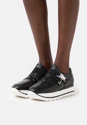 Melni ādas sporta apavi ar elastīgām siksnām un sudraba tonī metāla detaļām, ar resnu baltu gumijas zoli un elegantu, noapaļotu dizainu.