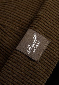 Tela de color marrón con relieve, que presenta una etiqueta de marca rectangular en gris con texto en cursiva blanca y la fecha de establecimiento.