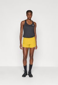 Mustmustelane tank top logoga, sobivalt kollaste lühikeste pükstega. Kangas on kerge ning pükstel on elastne vöökoht. Mustad spordialused kingad ja sokid lõpetavad ilme.