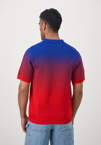 Punane ja sinine gradient lühikeste varrukate polo särk kraega, millel on tekstureeritud kudumine ja ümmargune logo detail vasakul varrukal.