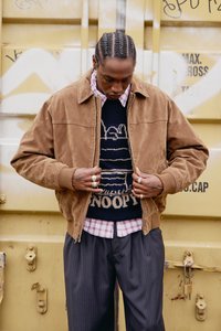 Barna velúr kabát gallérral, fekete pulóver fölött, amely Snoopy mintával díszített, alatta kockás ing. Az öltözéket csíkos nadrág egészíti ki.