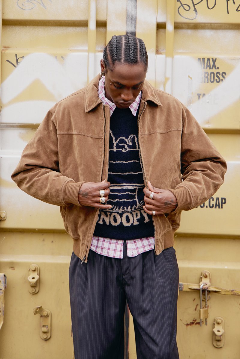 Barna velúr kabát gallérral, fekete pulóver fölött, amely Snoopy mintával díszített, alatta kockás ing. Az öltözéket csíkos nadrág egészíti ki.