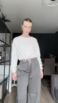 Fehér hosszú ujjú ing, megkötő derékkal és gyűrt érral, amelyet szürke csíkos nadrággal viselnek. Simát tapintás, laza stílus.