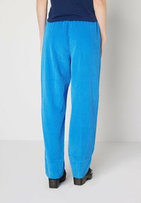 Siniset corduroypuvut, joissa on tekstuuri pinta, leveä lahje muotoilu ja joustava vyötärö, yhdistettynä mustiin paksupohjaisiin sandaaleihin.