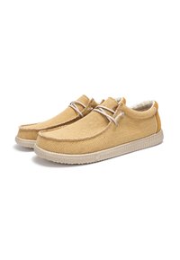 Zapatillas de tela color beige con una superficie texturizada, suela de goma beige y detalles mínimos de cordones. Presentan un pequeño acento marrón en el talón.