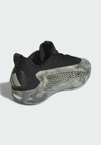 Scarpa sportiva nera con tomaia testurizzata, suola traslucida maculata e dettagli in rete, con particolare in fibra di carbonio sul tallone.