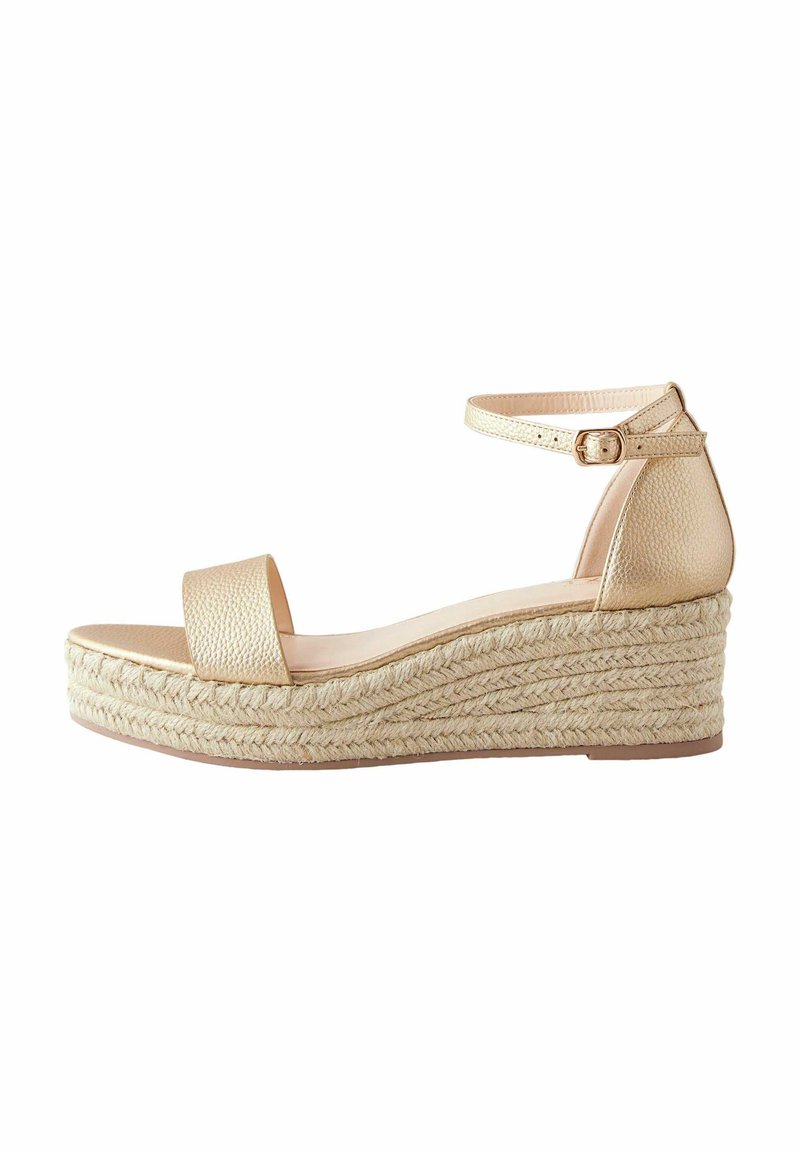 Zlatne wedge sandale s pletenom jutu platformom, s širokim prednjim remenom i podesivim remenom oko gležnja. Glatki, teksturirani gornji materijal.
