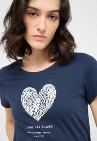 Námořnická modrá tričko s bílým květinovým srdcem a textem „J'aime les fleurs“ nad logem Mustang Jeans Company.