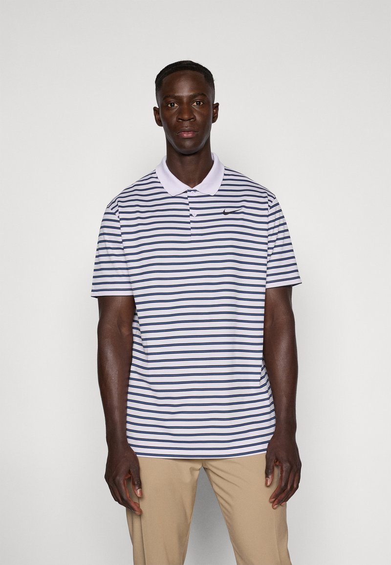 Striped polo shirt in light purple with navy horizontal stripes, featuring a collared neck and a small black Nike logo. Model wears beige pants.