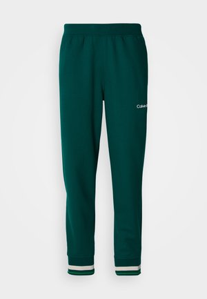 Zelené tepláky vyrobené z měkké látky, s tapered střihem, elastickým pasem a pruhovanými manžetami. Logo je umístěno po straně.