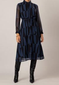 Navy blue long-sleeve dress with geometric pattern, button front, sheer fabric, belted waist, and a midi length. Worn with knee-high black boots.