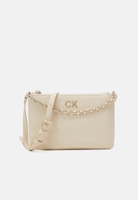 Beige nahkainen olkalaukku, jossa on kultaketju, vetoketjukiinnitys ja säädettävä hihna. Etupuolella on kohokuvioitu "CK" -logo.