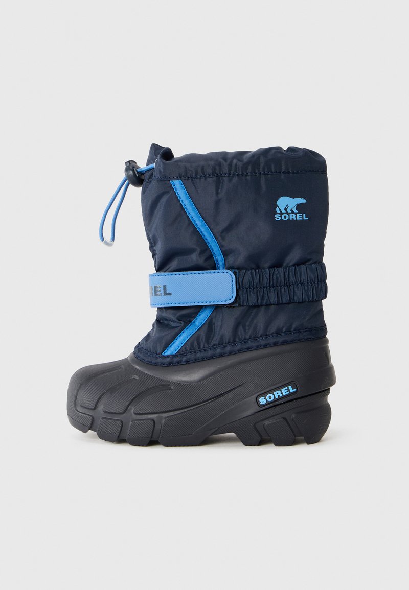 Botín de invierno para niño en color azul marino con suela de goma negra, correa ajustable azul y cierre con cordón, con el logo de Sorel en el lado.