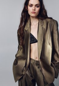 Metalgrøn jakkesæt i olivengrøn med en struktureret blazer og skræddersyede bukser. Fremhæver et tekstureret stof med en afslappet pasform og oversize silhuet.