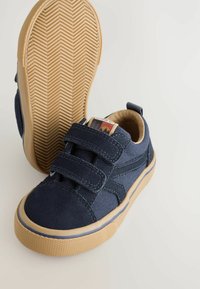 Baskets en toile bleu marine avec deux bandes Velcro, semelle en caoutchouc beige, coutures contrastantes et une étiquette avec un design de montagne.