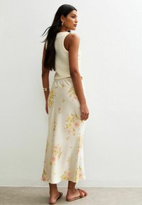 Gonna midi floreale in crema con stampe rosa e gialle, abbinata a un top in maglia crema e sandali piatti marroni. Tessuto morbido e leggero.