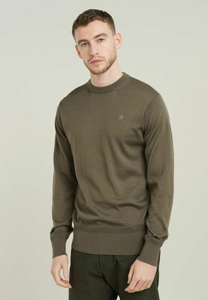 Maglione a maniche lunghe di colore verde oliva, con scollatura a girocollo e orlo a coste. Presenta un piccolo logo sul petto e una texture liscia.