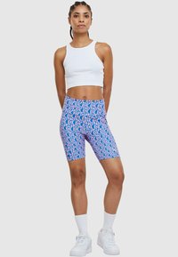 Modré a ružové vzorované cyklistické šortky majú elastický pás a priliehavý strih, spojené s bielym crop topom a bielymi teniskami.