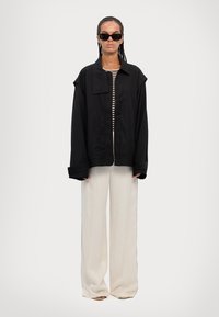 Black oversized jacket with a collar and long sleeves, worn over a striped top. Cream wide-leg pants. Accessories include dark sunglasses.