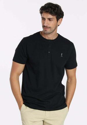 T-shirt henley noir à manches courtes avec trois boutons au cou, présentant un logo subtil sur la poitrine gauche et une texture de tissu lisse.