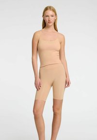 Hudfarvet tætsiddende tanktop og shorts, lavet af glat stof. Toppen har tynde stropper, mens shortsene er knælange med en sømløs skæring.