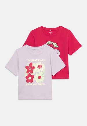 Deux t-shirts pour enfants à manches courtes, un violet clair avec des fleurs rouges et blanches et du texte, un rouge avec un graphique de cerise et des feuilles vertes.