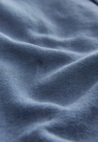 Material texturat într-o nuanță de albastru deschis, cu cute subtile și o țesătură fină. Materialul pare ușor, neted și ușor mat.