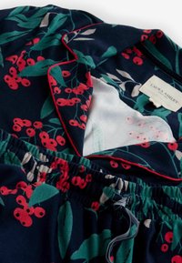 Námornícky pyžamo se vzorem červených květin, obsahující límeček, elastický pas a kontrastní červené lemování. Měkká, lehká tkanina.