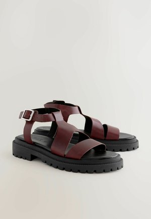 Bordové sandály s širokými koženými popruhy, otevřenou špičkou, nastavitelného zapínání na kotníku a robustní černou gumovou podrážkou s texturovaným vzorkem.