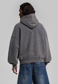 Haut à capuche gris surdimensionné avec une texture douce. Associé à un short en denim ample, mettant en valeur une silhouette décontractée.