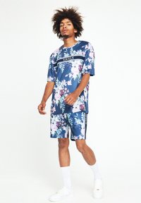 Blommig outfit med en marinblå kortärmad skjorta och matchande shorts. Tillverkad av ett mjukt, lätt material med kontrasterande svarta detaljer.