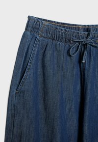 Ciemnoniebieskie spodnie dżinsowe z elastycznym pasem, sznurkiem do wiązania i widoczną boczną kieszenią na jasnym tle.