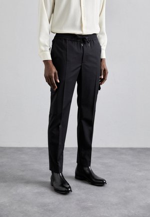 Pantalons noirs fuselés avec une taille élastique et un cordon de serrage, dotés de poches latérales et d'une texture de tissu lisse, associés à des bottines noires.