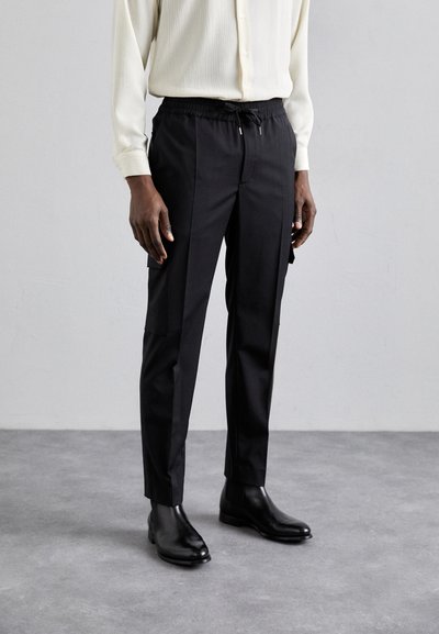 Schwarze tapered Hosen mit elastischem Bund und Kordelzug, ausgestattet mit Seitentaschen und glattem Stoff, kombiniert mit schwarzen Stiefeletten.