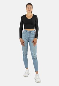 Schwarzes Langarm-Crop-Top, kombiniert mit hellblauen High-Waisted-Jeans. Das Model trägt weiße Sneakers und schlichte Ohrringe. Glatte Textur.