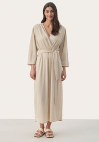 Beige gestreiftes Wickelkleid mit langen Ärmeln, in der Taille gebunden und aus weichem Material; kombiniert mit hellen Sandalen mit einer Schnalle.