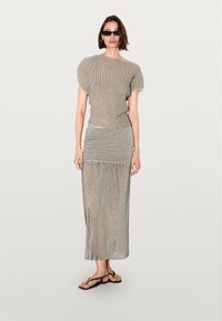 Stribet to-delt sæt i sort og creme. Toppen har en løs pasform med dolmanærmer, og nederdelen er lang med en tætsiddende talje og flydende kant.