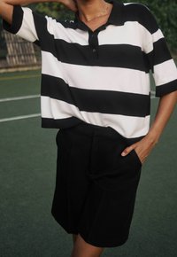 Polo a righe bianche e nere con maniche corte, patta dei bottoni e pantaloni corti neri. Il tessuto sembra morbido con una vestibilità rilassata.