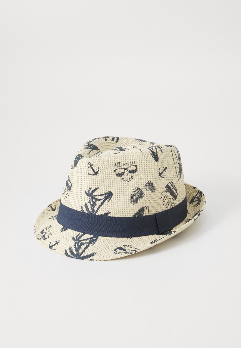 Stråhatt med marineblå bånd som har trykte design av ankere, solbriller og tropiske blader mot en beige bakgrunn.