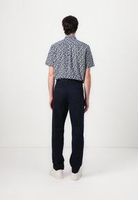 Korte mouwen shirt in marineblauw met wit bladmotief, gecombineerd met donkergekleurde broeken en witte sneakers, vanuit de achterkant getoond.